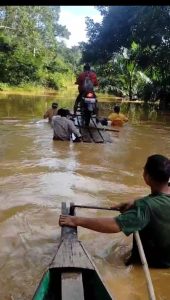 Debit Air Meningkat, Bhabinkamtibmas Polsek Sayan Bantu Warga Melewati Jalanan yang Terendam Banjir